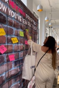 A wall with several names and a women writing something og peice of paper for wall
